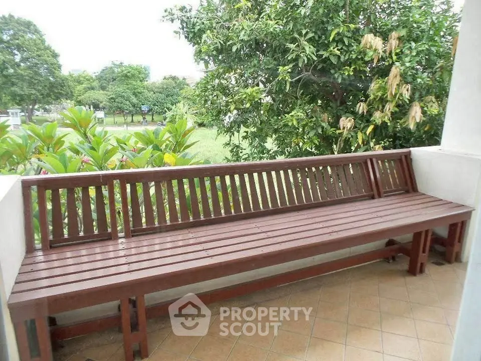 Charming garden view from a cozy balcony with wooden bench seating.