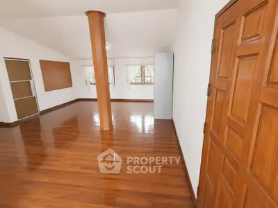 Spacious empty room with polished wooden floors and large windows, ideal for customization.