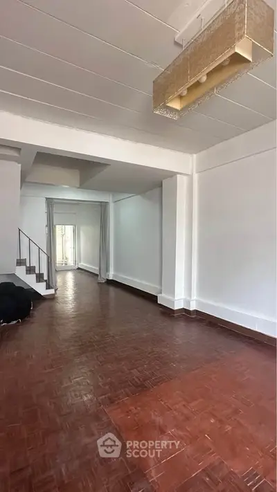 Spacious living room with wooden flooring and modern lighting, ideal for family gatherings.