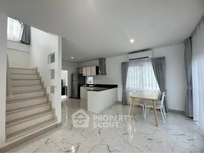 Modern open-plan living area with sleek kitchen and elegant staircase, featuring marble flooring and ample natural light.