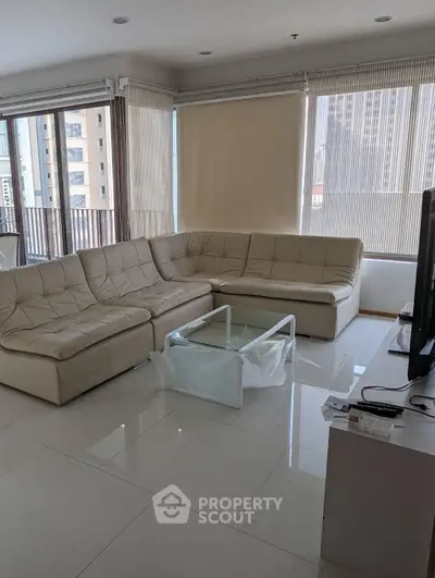 Spacious living room with large windows and modern furniture in a high-rise apartment.