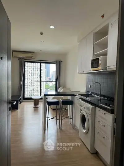 Modern open-layout kitchen with washing machine and city view in high-rise apartment.