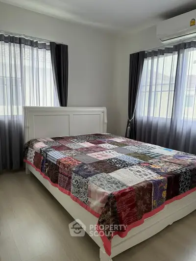 Cozy bedroom with stylish patchwork quilt and natural light from large windows.