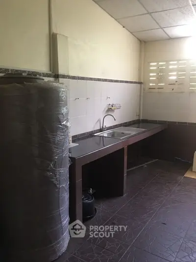 Spacious kitchen with tiled flooring and large water heater, ideal for modern living.
