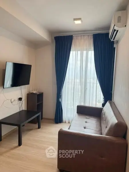 Cozy living room with modern sofa, wall-mounted TV, and large window with blue curtains.