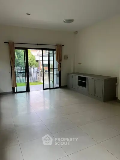 Spacious living room with sliding glass doors leading to a garden view, featuring neutral tones and ample natural light.