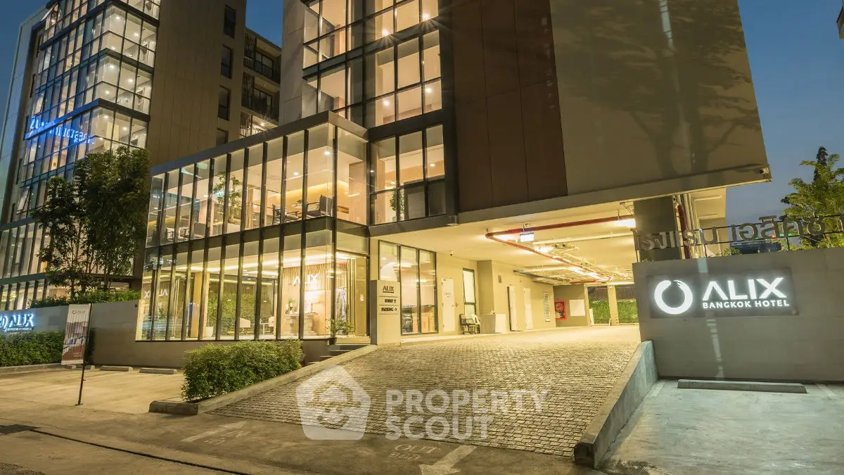 Modern hotel exterior with illuminated entrance and sleek glass facade at dusk.