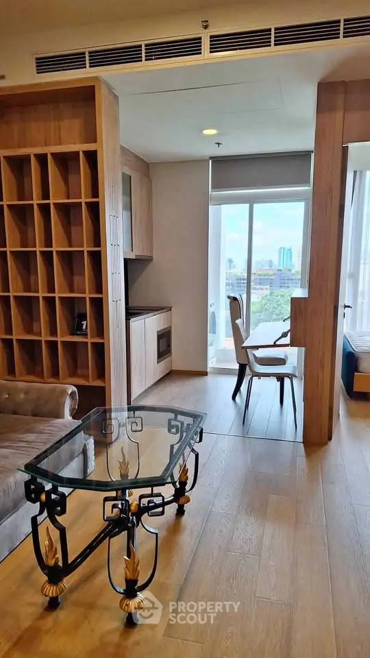 Modern living room with elegant glass table and built-in wooden shelving, offering a bright city view.
