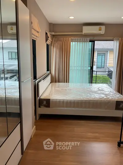 Modern bedroom with large window and wooden flooring in a stylish apartment.
