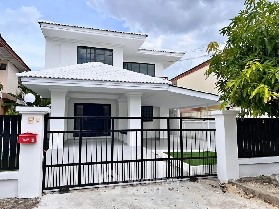 Stunning modern white two-story house with gated entrance and lush greenery, perfect for family living.