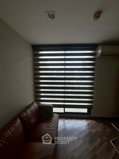 Modern living room with stylish blinds and leather sofa, featuring wooden flooring and air conditioning.