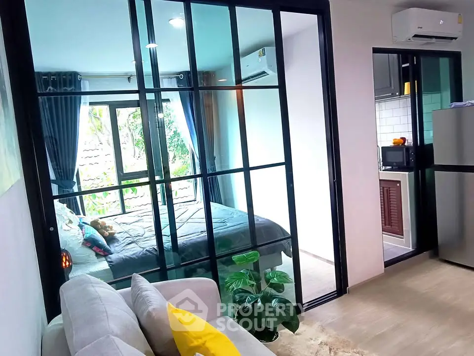 Modern apartment with glass partition, cozy living area, and compact kitchen, featuring a bright bedroom view.
