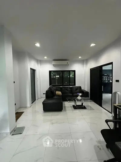 Spacious modern living room with sleek black furniture and elegant white tile flooring.