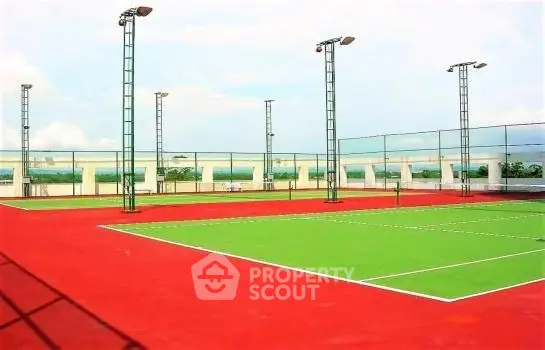 Spacious rooftop tennis court with vibrant red and green surface, ideal for sports enthusiasts.