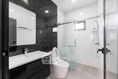 Modern bathroom with sleek black and white design, featuring a glass shower and stylish fixtures.