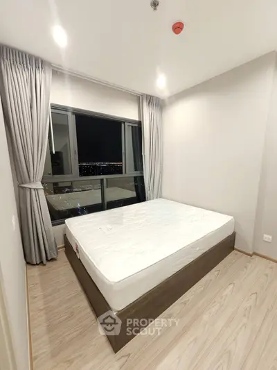 Modern bedroom with large window and city view, featuring a comfortable bed and elegant curtains.