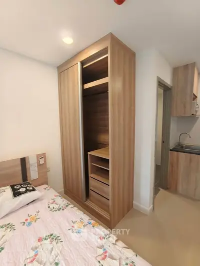 Modern bedroom with built-in wardrobe and partial kitchen view in stylish apartment.