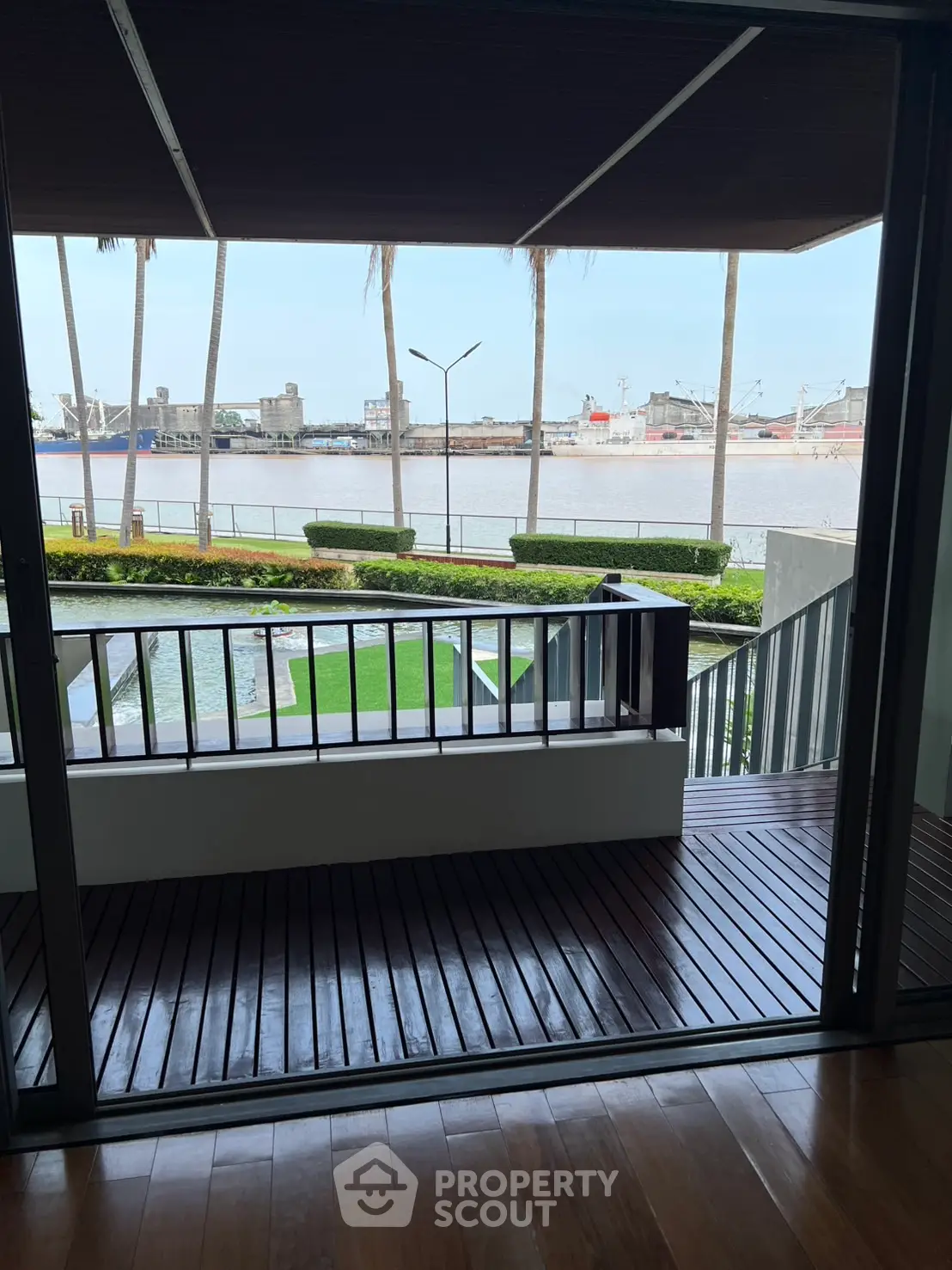 Stunning waterfront view from a modern balcony with wooden flooring and lush greenery.
