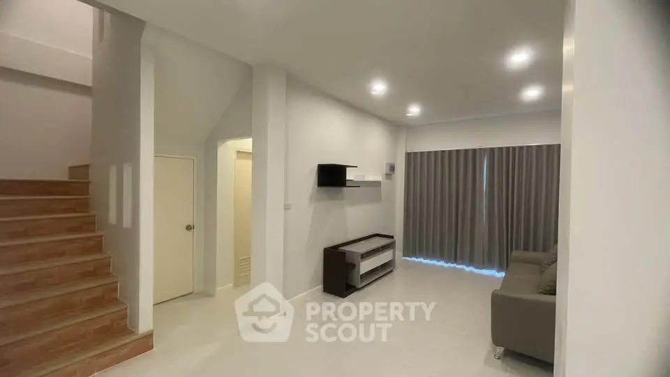 Modern living room with sleek design and neutral tones, featuring a staircase and stylish furniture.