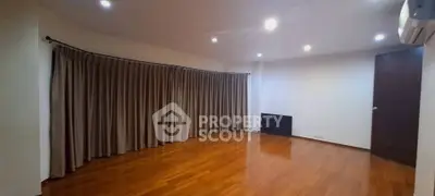 Spacious empty room with wooden flooring and large window draped with curtains, ideal for customization.