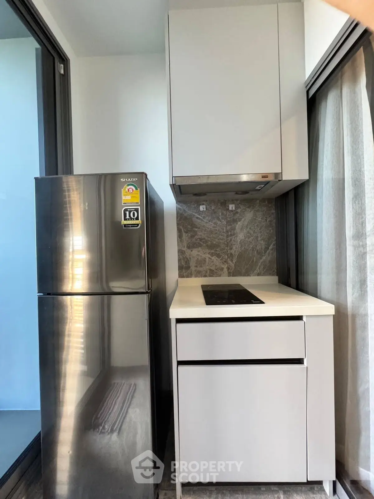 Modern compact kitchen with sleek fridge and induction cooktop in cozy apartment.
