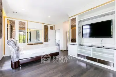 Spacious bedroom with modern decor and large TV, featuring elegant wood flooring and ample storage.