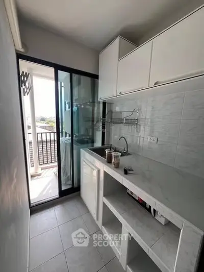 Modern kitchen with sleek white cabinets and balcony access, featuring a compact yet functional design.