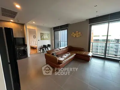 Spacious modern living room with leather sofa and large windows offering city views.