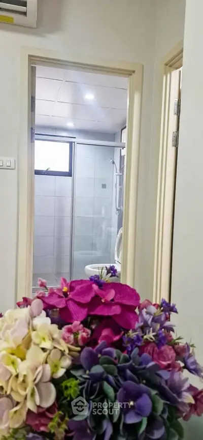 Modern bathroom view from hallway with elegant floral arrangement in foreground.