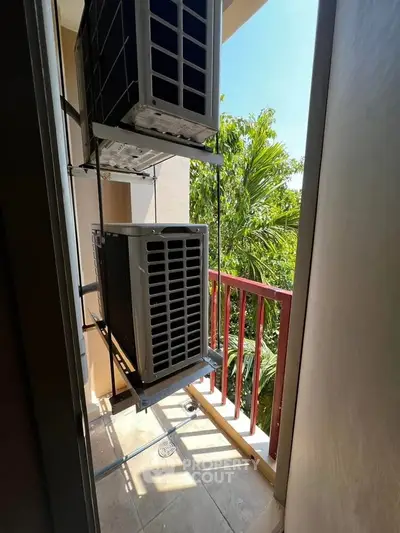 Compact balcony with air conditioning units and lush greenery view