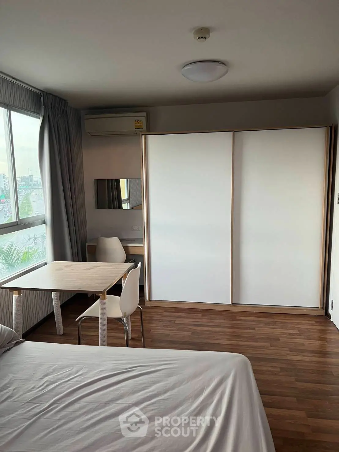 Modern bedroom with wooden flooring, large window, and sleek sliding wardrobe doors.