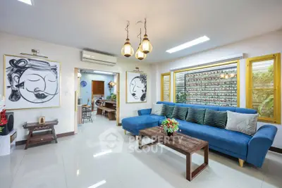 Stylish living room with modern decor, blue sofa, and artistic wall paintings in a bright, airy space.