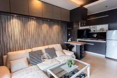 Modern living room with stylish decor and open kitchen layout, featuring sleek furniture and ambient lighting.