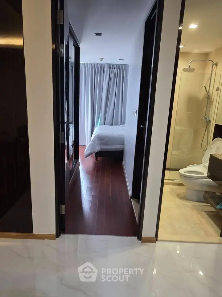 Modern apartment hallway leading to a cozy bedroom and sleek bathroom with glass shower.