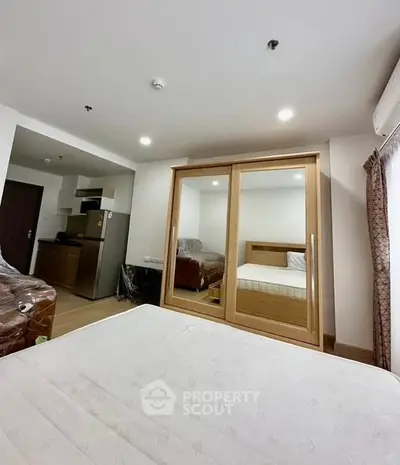 Modern bedroom with mirrored wardrobe and compact kitchen area in stylish apartment.