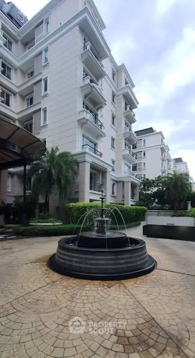 Elegant residential building with fountain and lush greenery in a luxurious setting.