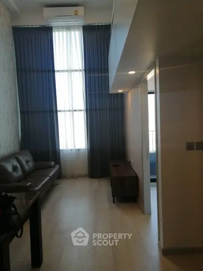 Modern living room with high ceiling and large window, featuring a sleek sofa and elegant decor.