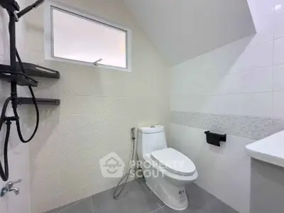 Modern bathroom with sleek fixtures and neutral tiles, featuring a toilet and shower area.