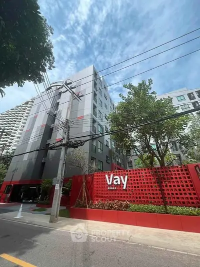 Modern apartment building exterior with red accents and lush greenery, ideal urban living.