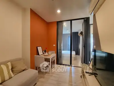 Modern living room with orange accent wall and glass partition leading to bedroom
