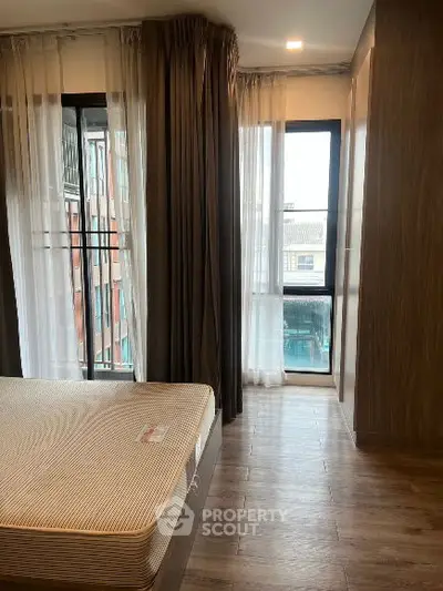 Spacious bedroom with large windows and elegant curtains, offering ample natural light and a cozy atmosphere.