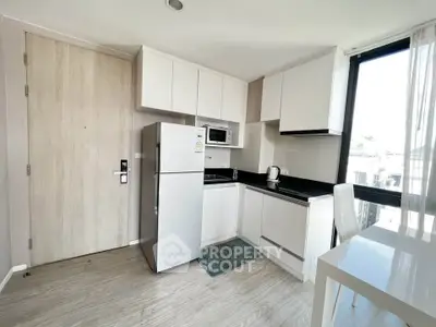 Modern kitchen with sleek white cabinets, stainless steel fridge, and large window for natural light.