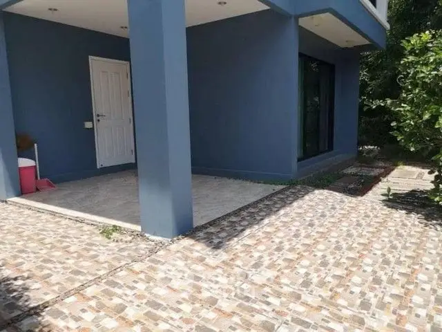 Modern blue exterior with tiled patio and lush greenery.