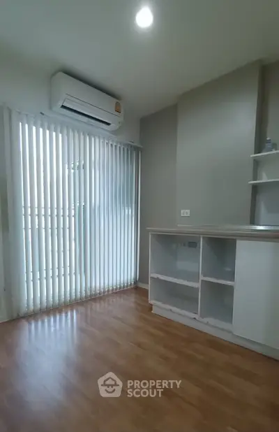 Modern apartment interior with wooden flooring and air conditioning, featuring a compact kitchen area.