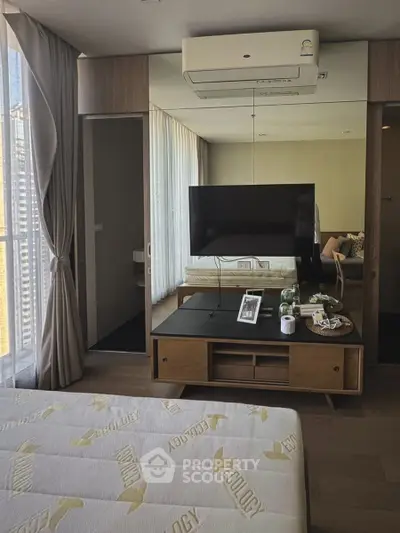 Modern bedroom with large window, mirrored wardrobe, and wall-mounted TV in a stylish apartment.