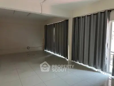 Spacious empty room with tiled flooring and large windows covered by gray curtains.