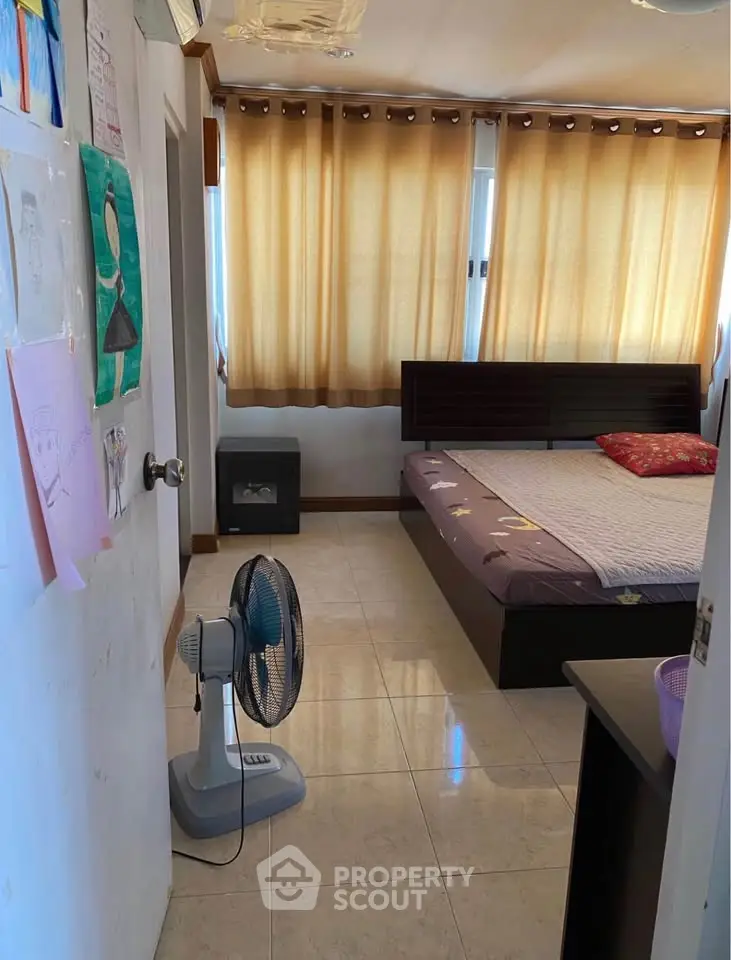 Cozy bedroom with large windows and natural light, featuring a comfortable bed and fan for a relaxing atmosphere.