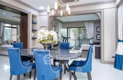 Elegant dining room with blue chairs and marble table, open layout to living area, modern chandelier.