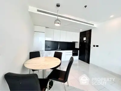 Modern kitchen with sleek black and white design, featuring a round marble dining table and stylish chairs.