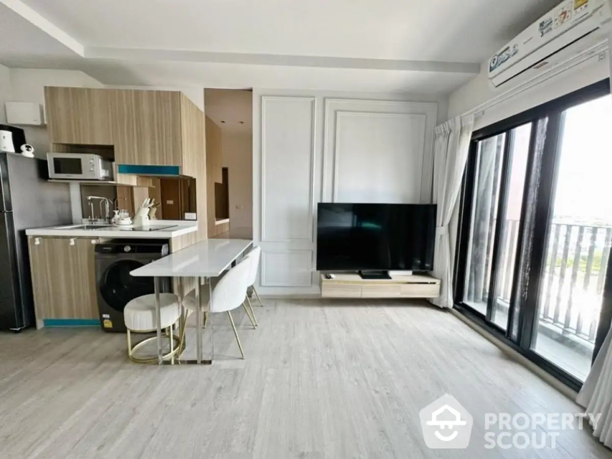 Modern open-plan living room with sleek kitchen, large TV, and balcony access, perfect for contemporary living.